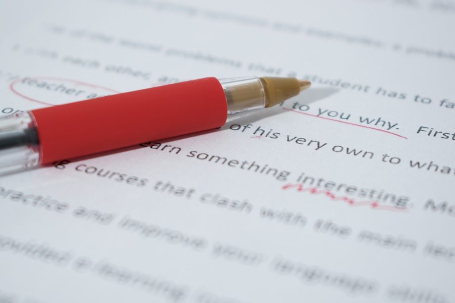Picture of a red pen correcting an essay for a blog post about how to write better essays for high school.